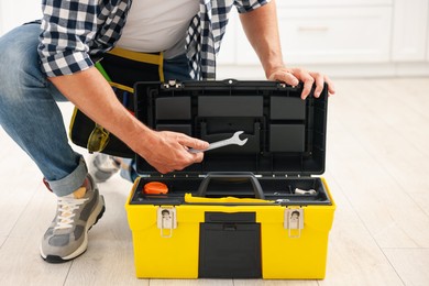Photo of Man taking wrench from tool box indoors, closeup