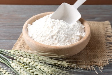 Photo of Flour in bowl and green wheat spikes on wooden table, closeup