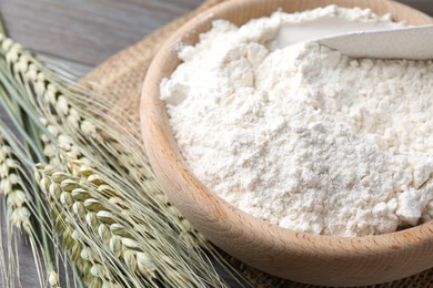 Photo of Flour in bowl and green wheat spikes on table, closeup