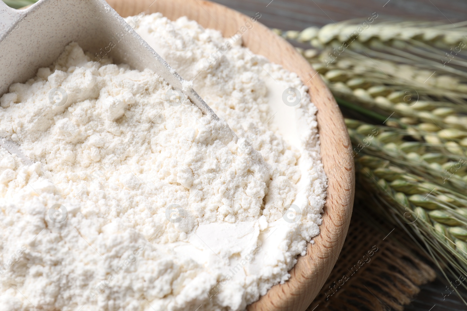 Photo of Flour in bowl and green wheat spikes on table, closeup