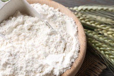 Photo of Flour in bowl and green wheat spikes on table, closeup