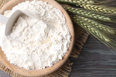 Photo of Flour in bowl and green wheat spikes on wooden table, flat lay