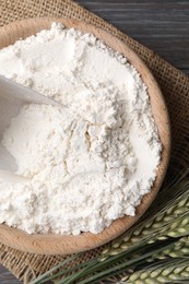 Photo of Flour in bowl and green wheat spikes on wooden table, flat lay
