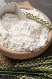 Photo of Flour in bowl and green wheat spikes on table, closeup