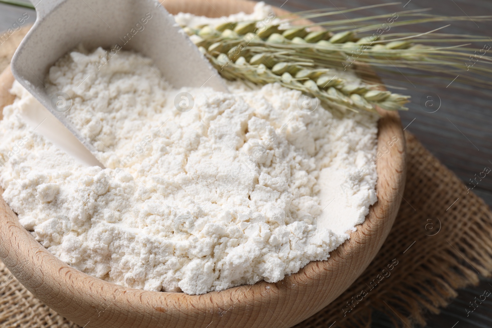 Photo of Flour in bowl and green wheat spikes on table, closeup