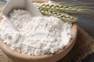 Photo of Flour in bowl and green wheat spikes on table, closeup