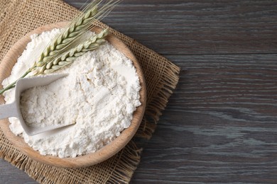 Photo of Flour in bowl and green wheat spikes on wooden table, top view. Space for text