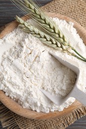 Photo of Flour in bowl and green wheat spikes on wooden table, top view