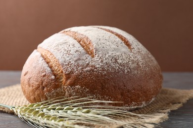 Photo of Fresh bread and green wheat spikes on wooden table, closeup