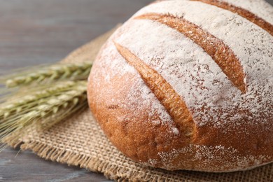 Photo of Fresh bread and green wheat spikes on wooden table, closeup