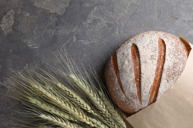 Photo of Fresh bread and green wheat spikes on grey table, flat lay