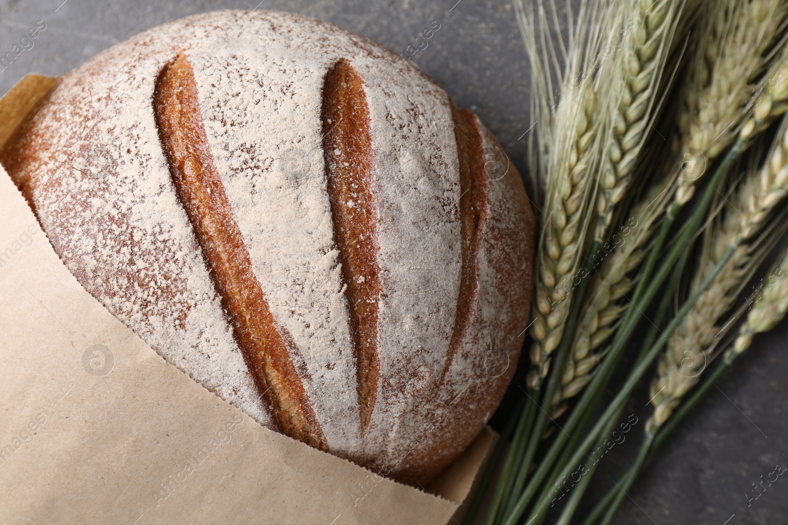 Photo of Fresh bread and green wheat spikes on grey table, flat lay