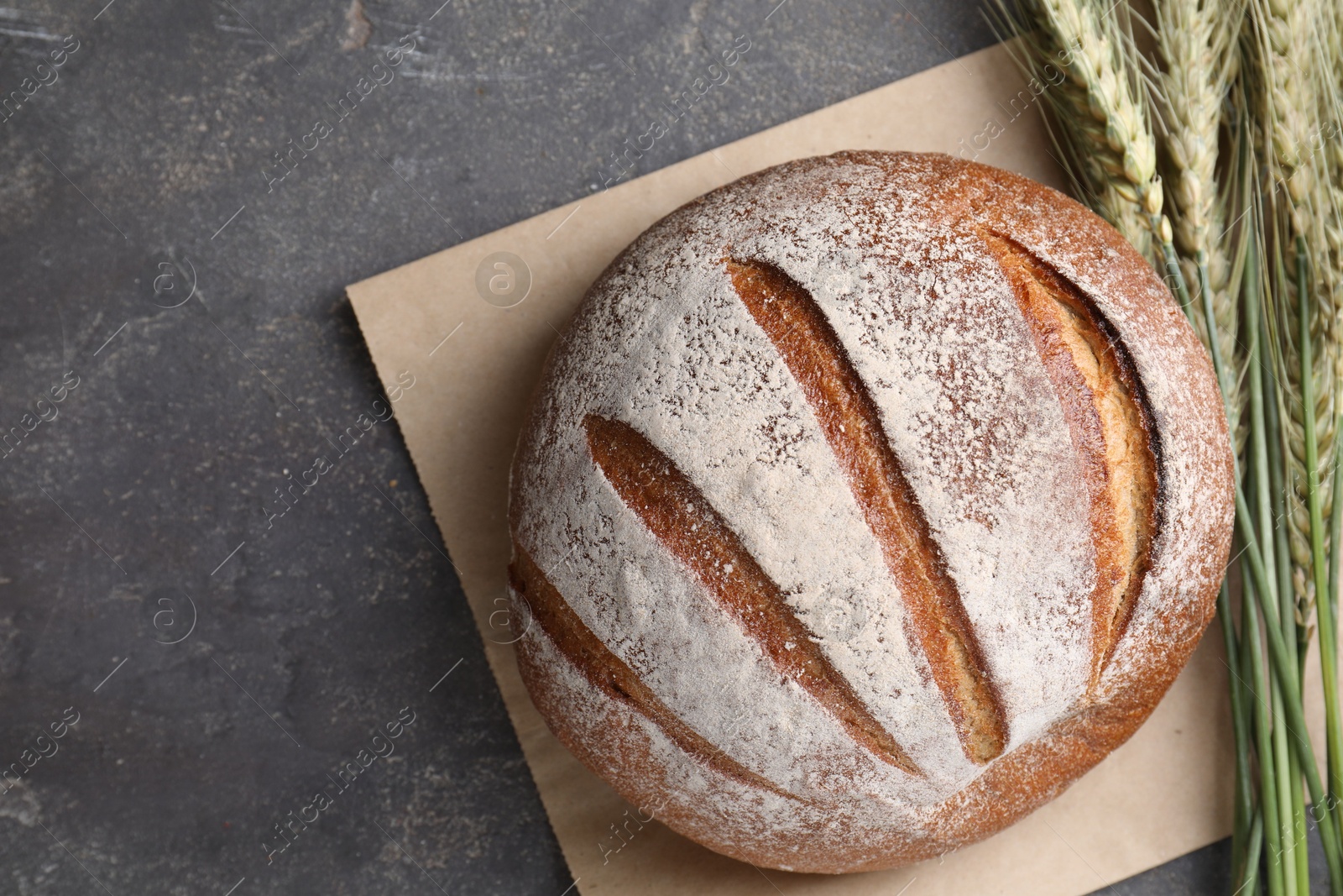 Photo of Fresh bread and green wheat spikes on grey table, flat lay. Space for text