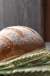Photo of Fresh bread and green wheat spikes on table, closeup
