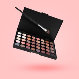 Image of Eyeshadow palette and brush in air against pink background. Makeup cosmetics