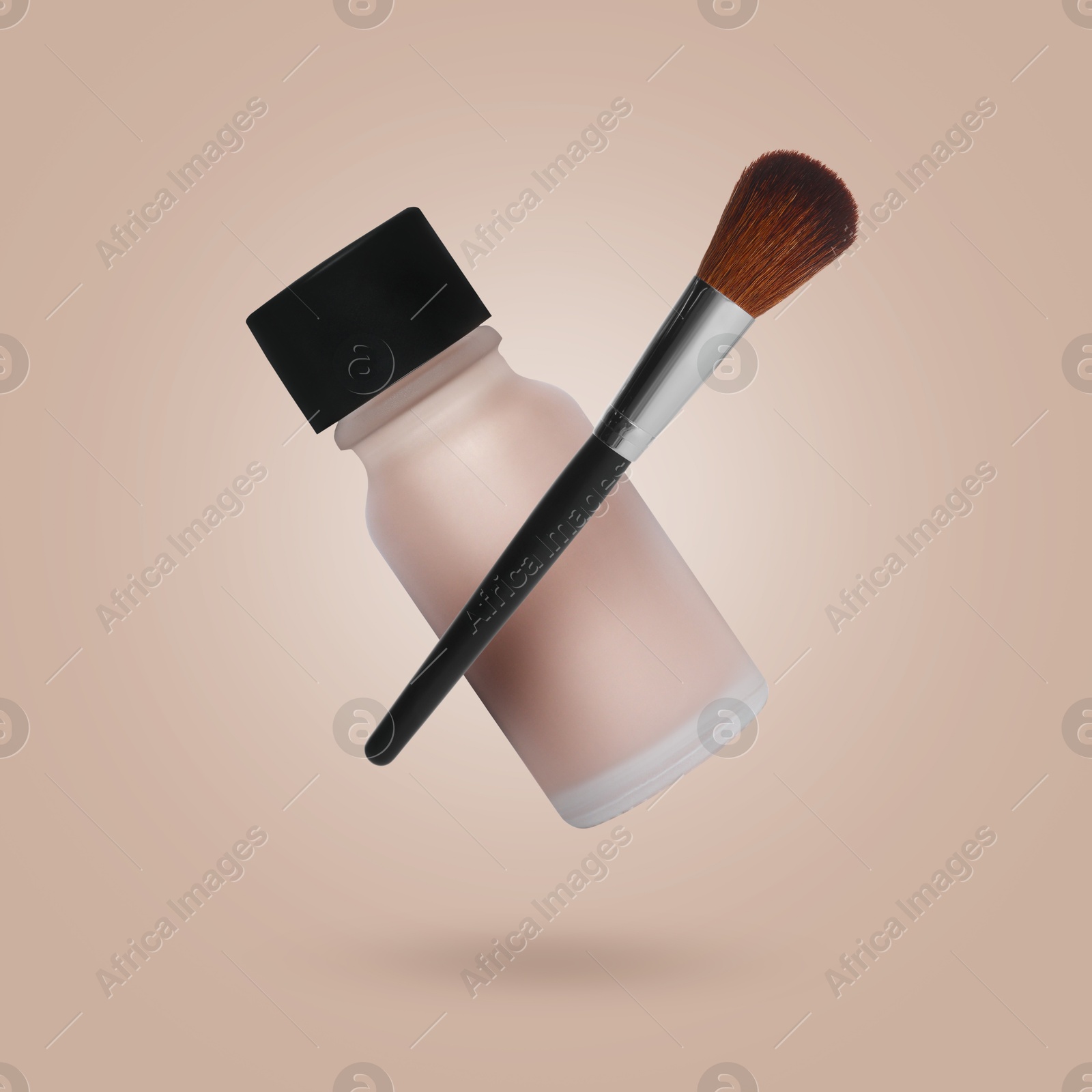 Image of Liquid skin foundation and brush in air against dark beige background. Makeup cosmetics