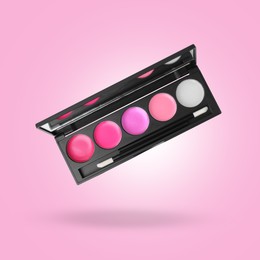 Image of Lip palette with brush in air against pink background. Makeup cosmetics