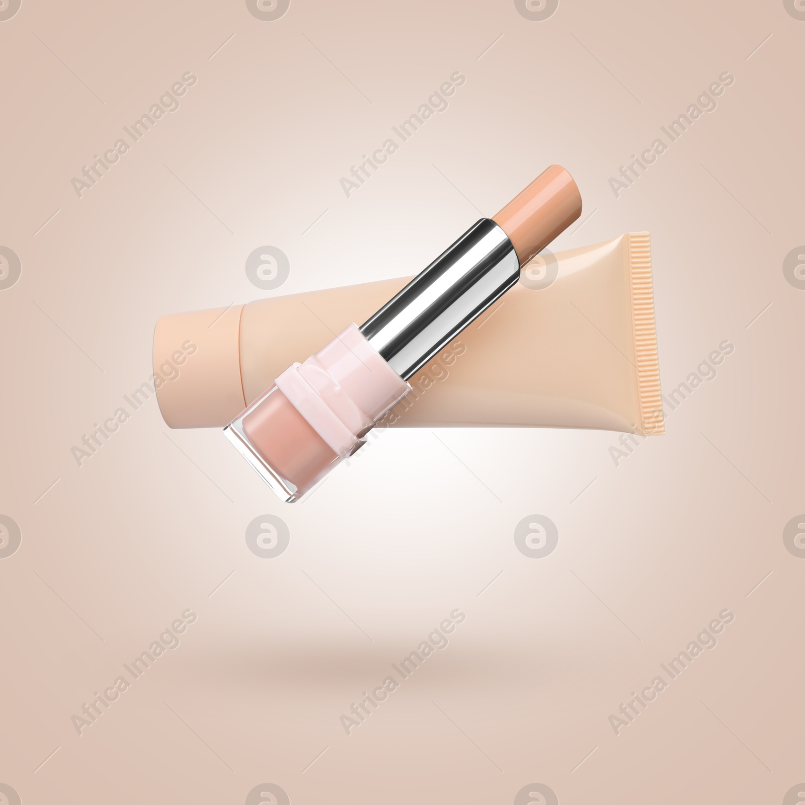 Image of Liquid skin foundation and stick concealer in air against dark beige background. Makeup products