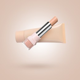 Image of Liquid skin foundation and stick concealer in air against dark beige background. Makeup products