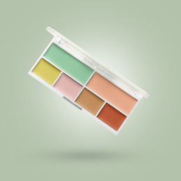 Image of Concealer palette in air against sage color background. Makeup cosmetics