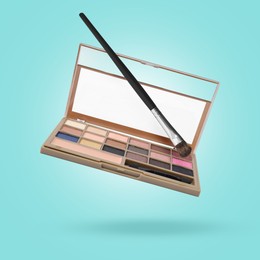Image of Eyeshadow palette and brush in air against light blue background. Makeup cosmetics