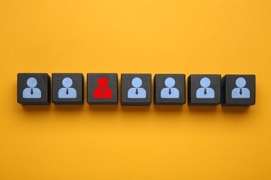 Image of Dismissal. Black cube with red human icon among others with blue ones on orange background, top view