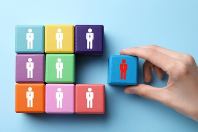 Image of Dismissal. Woman taking cube with red human icon among others with white ones on light blue background, top view
