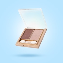 Image of Eyeshadow and applicator in air against light blue background. Makeup cosmetics