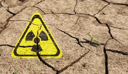 Image of Yellow radioactive sign on cracked dry earth, closeup. Radiological pollution