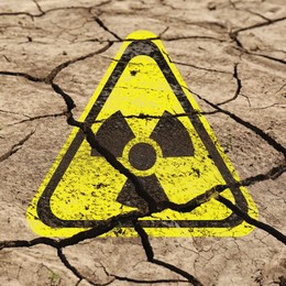 Image of Yellow radioactive sign on cracked dry earth, closeup. Radiological pollution