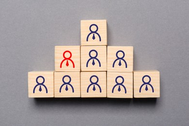 Image of Dismissal. Cube with red human icon among others with blue ones on grey background, top view