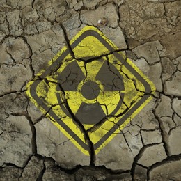 Image of Yellow radioactive sign on cracked dry earth, closeup. Radiological pollution