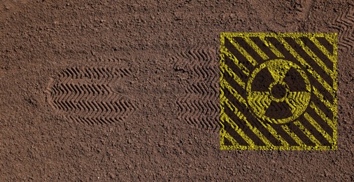 Image of Yellow radioactive sign on brown ground with shoes tracks, top view. Radiological pollution
