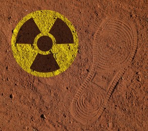 Image of Yellow radioactive sign on brown ground with shoes track, top view. Radiological pollution