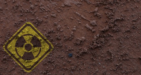 Image of Yellow radioactive sign on brown ground, top view. Radiological pollution