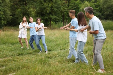 Photo of Team building. Group of happy people playing tug of war with rope outdoors