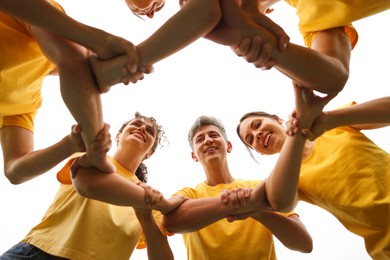 Photo of Team building. Group of happy people joining hands outdoors, bottom view