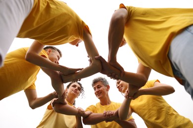 Photo of Team building. Group of happy people joining hands outdoors, bottom view