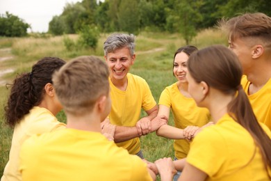 Photo of Team building. Group of happy people joining hands outdoors