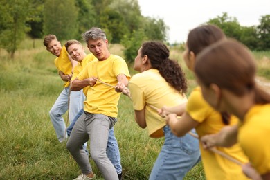Photo of Team building. Group of happy people playing tug of war with rope outdoors
