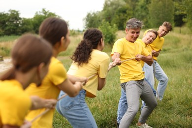 Photo of Team building. Group of happy people playing tug of war with rope outdoors