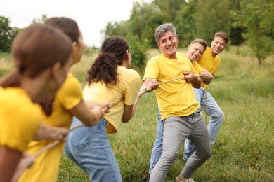 Photo of Team building. Group of happy people playing tug of war with rope outdoors