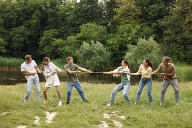 Photo of Team building. Group of happy people playing tug of war with rope outdoors