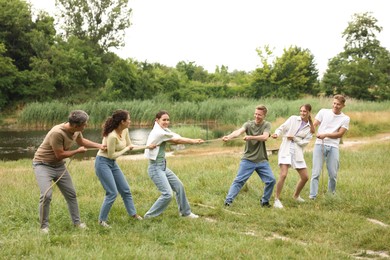 Photo of Team building. Group of happy people playing tug of war with rope outdoors
