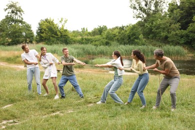 Photo of Team building. Group of happy people playing tug of war with rope outdoors