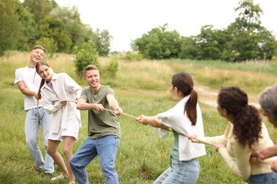 Photo of Team building. Group of happy people playing tug of war with rope outdoors