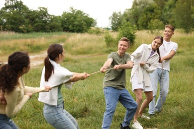Photo of Team building. Group of happy people playing tug of war with rope outdoors