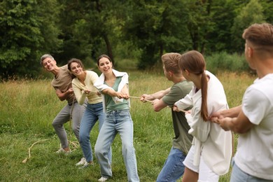 Photo of Team building. Group of happy people playing tug of war with rope outdoors