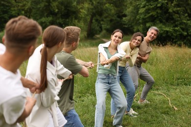 Photo of Team building. Group of happy people playing tug of war with rope outdoors