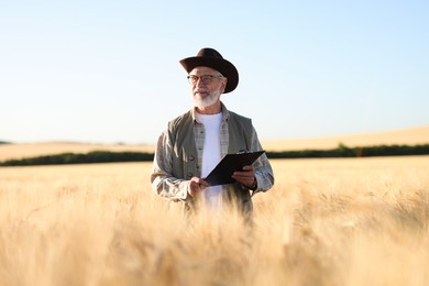 Photo of Senior farmer with clipboard in field of ripe wheat outdoors